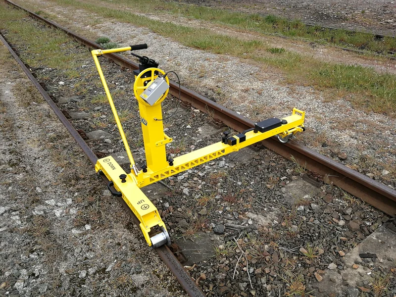 The measuring arm reaches to the far rail; one person lifts the trolley onto the track and sets it to the gauge