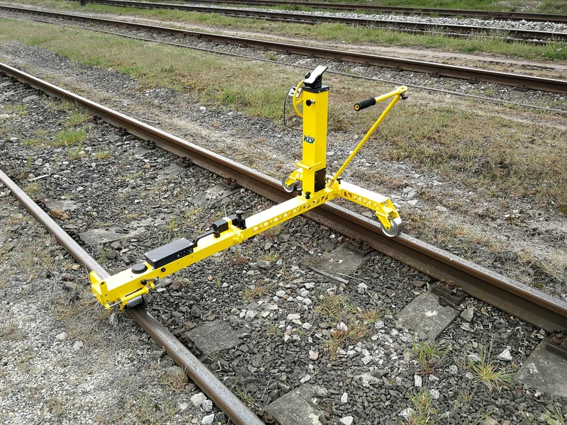 In measuring position: the beam spans the track, the laser distance meter and the handlebar sit on the mast, and one person pushes it