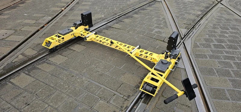 A rail profile camera over each grooved rail; the solid body keeps the trolley on the rails through tight curves and crossings
