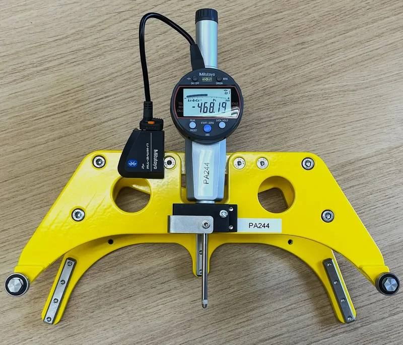 SPIDER held against a rail vehicle wheel in the workshop: a yellow three-arm frame with the digital indicator on top.